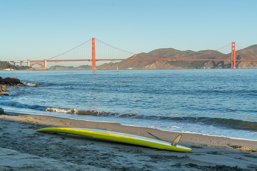 View of people enjoying the bay, swimming at Chrissy Field on a calm summer day with the famous Golden Gate Bridge in the background.
A surfboard in the foreground.