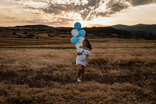 Beautiful young pregnant woman holding blue balloons to revile baby's gender on a sunny summer day in nature