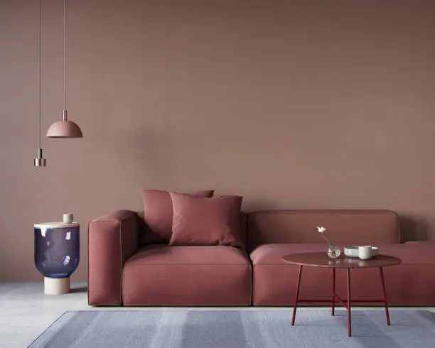 Living room interior with a large red sofa, metal and glass tables, a chandelier and a blue carpet on a concrete floor