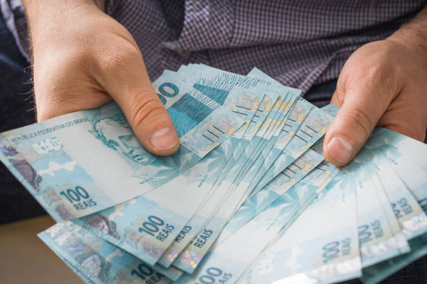 человек, д�ержащий в руке пачку высокой стоимости бразильских денег - human hand beak currency stack стоковые фото и изображения