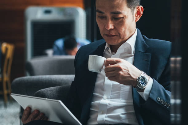Successful businessman drinking cup of coffee and looking at tablet