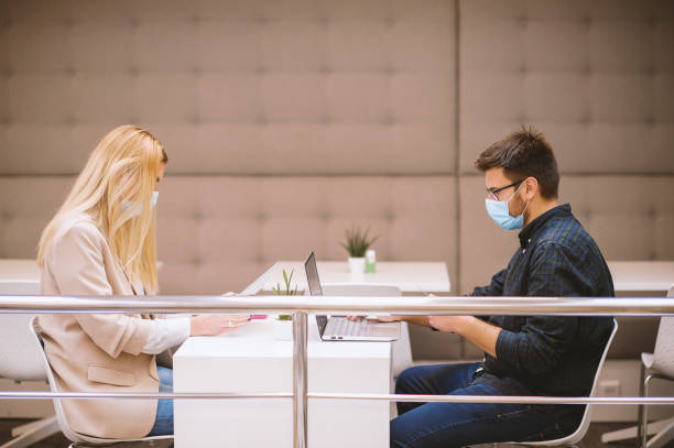 istock Two business people with protective face masks working together in small modern office, keeping safe distance. 1283075444