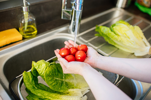 Woman washing fresh tomatoes and  lettuce under the tap