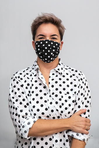 Female wearing polka dots shirt and mask in black and white. Portrait with mask, smiling behind the mask. Studio shot for coronavirus awareness