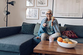 Happy senior woman snacking an apple and watching TV at home
