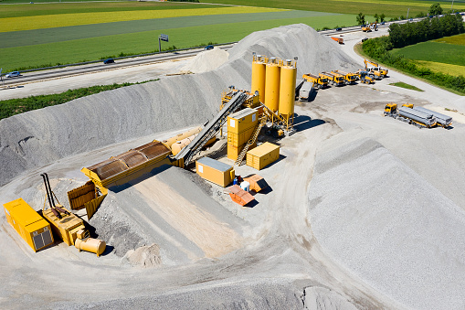 A large stone crusher plant with silos and construction machinery  used for highway renovation, aerial view.