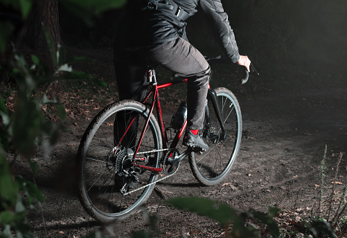 Cyclist on a forest trail at night. Man on bicycle in the dark forest close up. Active lifestyle concept. Hard shadows from flash.