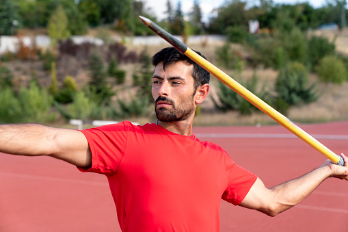 man athlete about to throw a javelin in the stadium. sportsman practising javelin throw against bright blue sky with clouds