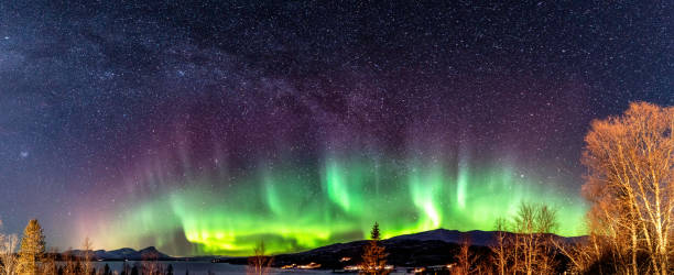 istock Panoramic view of multicolored strong lighting Aurora curved above Scandinavian mountains and frozen lake, very cold winter night, deep clear sky 1283093490