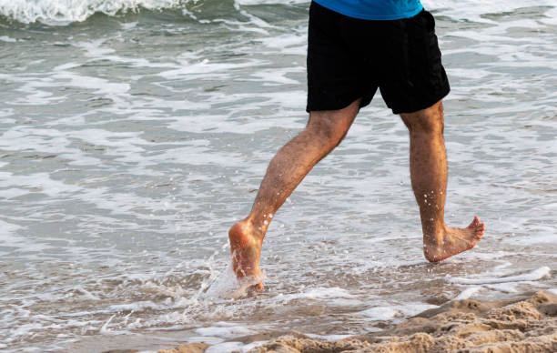 istock Rear view of barefoot runner running in water 1283094357