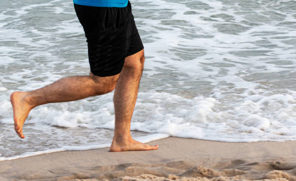 istock Side view of man running barefoot on beach next to water 1283094369