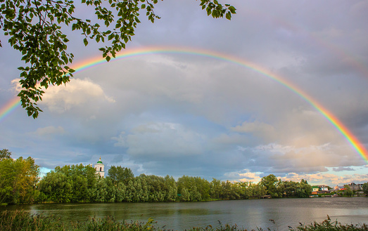 Landscape with a rainbow over a pond and a forest near the village.