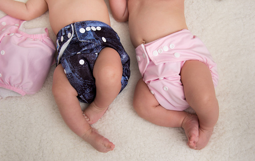 Baby lying on a bed wearing a cloth diaper and a teddy bear