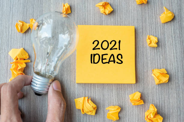 istock 2021 Idea words on yellow note and crumbled paper with Businessman holding lightbulb on wooden table background. New Year New Start Creative, Innovation, Imagination, Resolution and Goal concept 1283112188