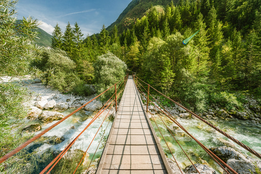 Suspension wooden bridge over clear mountain river and evergreen trees.