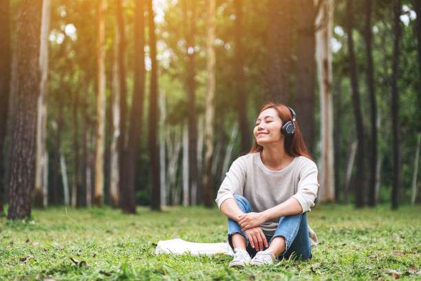 若いアジアの女性は、公園で幸せとリラックス感を持つヘッドフォンで音楽を聴いて楽しむ - young adult technology beautiful singing ストックフォトと画像