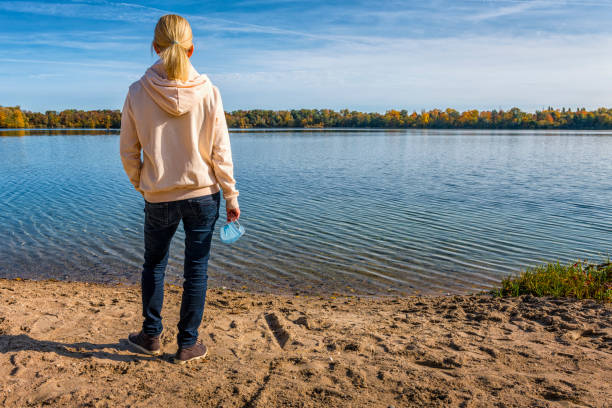 istock woman at a lake holding a protective face mask 1283128533