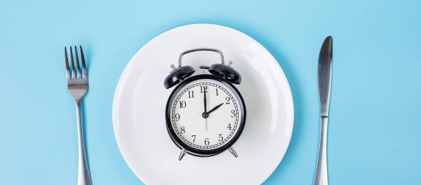 istock Top view alarm clock on white plate with knife and fork on blue background. Intermittent fasting, Ketogenic dieting, weight loss, meal plan and healthy food concept 1283129466