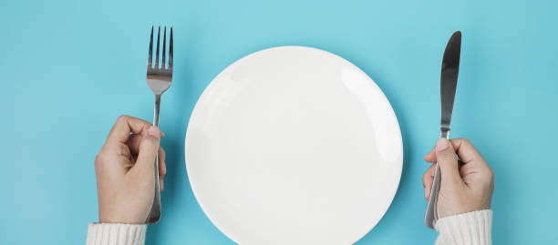 istock Hands holding knife and fork above white plate on blue background., dieting, weight loss, dining and kitchenware concept 1283129473
