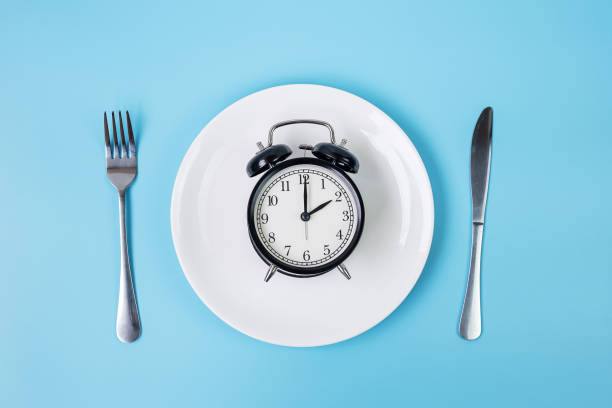 istock Top view alarm clock on white plate with knife and fork on blue background. Intermittent fasting, Ketogenic dieting, weight loss, meal plan and healthy food concept 1283129776