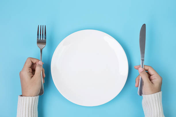 istock Hands holding knife and fork above white plate on blue background., dieting, weight loss, dining and kitchenware concept 1283129777