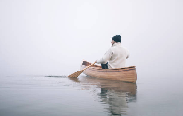 Winter canoeing Rear view of man paddling canoe in the winter, copy space. rowboat stock pictures, royalty-free photos & images