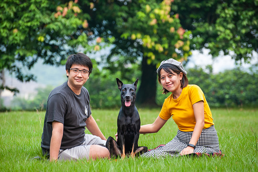 Young Asian couple spending quality time with their pet dog at community park in the morning.