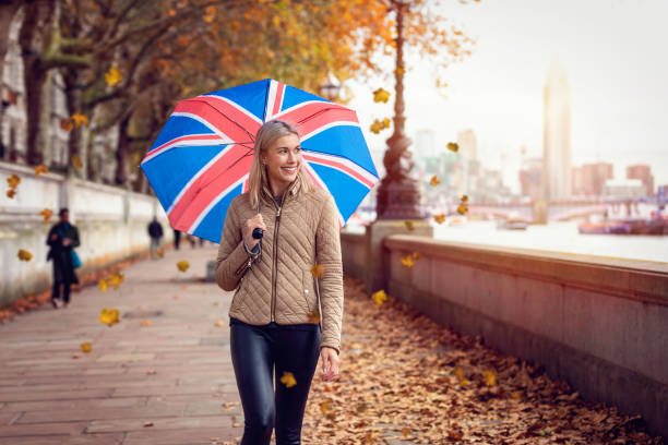 una donna con un ombrello di souvenir bandiera britannica passeggia lungo il lungofiume di londra, regno unito - british flag flag london england england foto e immagini stock