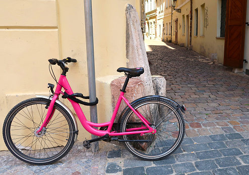 Pink bicycle leaning against the wall in the street of Prague city, Czech Republic, a typical street of the old town in the background. It is locked to the lamppost.