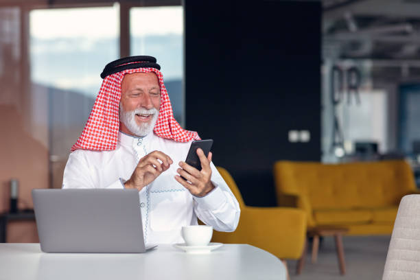 hombre de negocios árabe confiado y sonriendo en la oficina usando portátil. - headscarf islam senior adult east fotografías e imágenes de stock