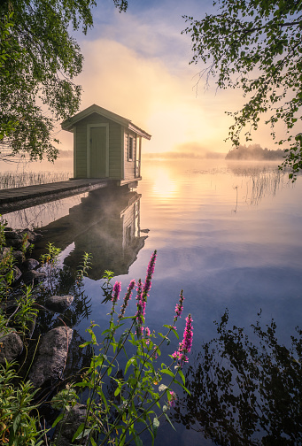 Beautiful morning landscape with little swim cottage, pier and foggy sunrise in lakeside Finland