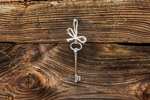 One old rusty key hanging on a nail on wooden wall background. Vintage style, copy space