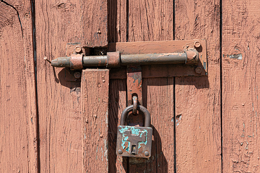 Old rusted grungy wooden garage door with latch and padlock. Close up of rusty vintage lock on closed door