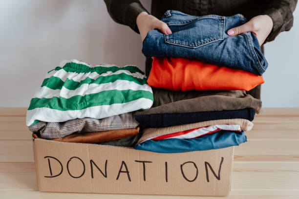 istock Woman folding and packing used clothes into cardboard donation box. 1283154271