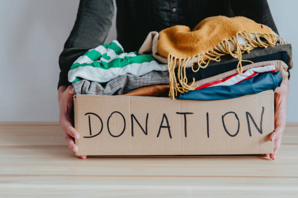 Woman holding cardboard donation box full with folded clothes. stock photo