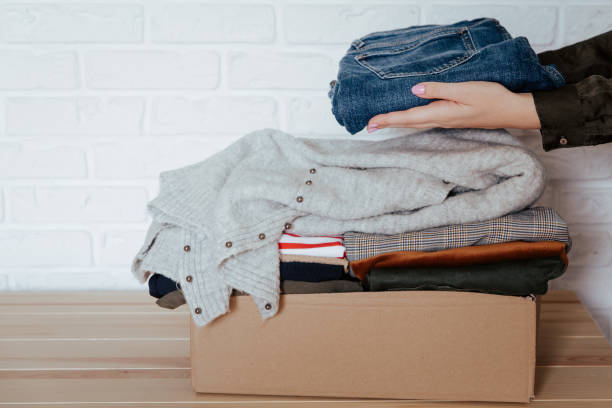 istock Woman folding and packing used clothes into cardboard donation box. 1283154284