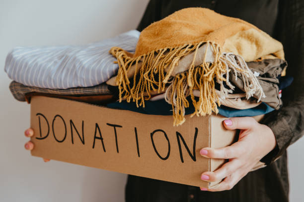 istock Woman holding cardboard donation box full with folded clothes. 1283154330