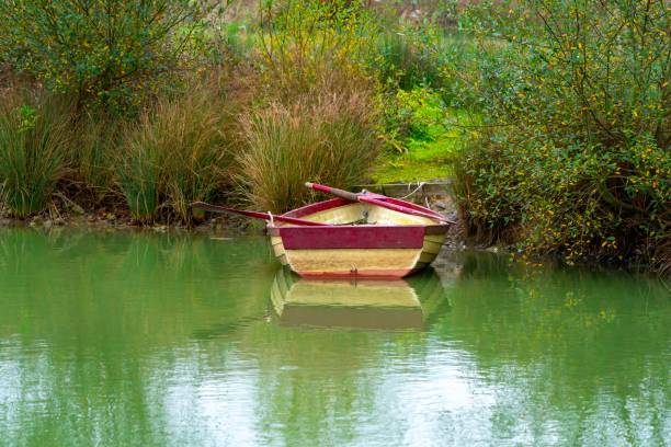 Small red and yellow rowing boat sitting in the water in a country lake taken in Beckington Frome Somerset England on the 30th October 2020