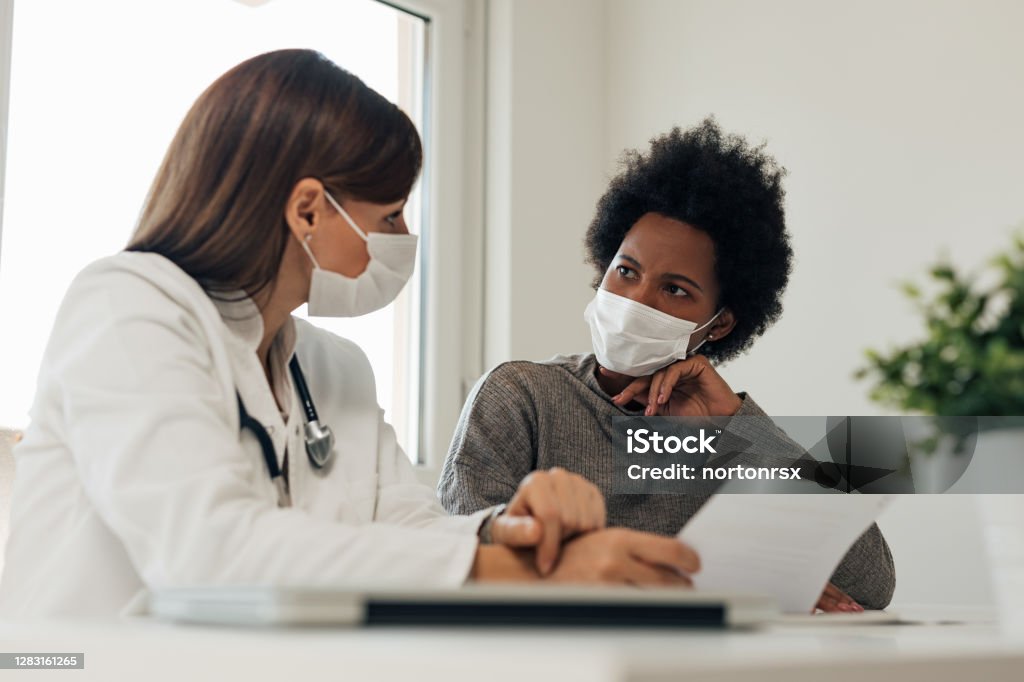 Talking about patients diagnosis. Both of these woman wearing mask, doctor and patient. Doctor Stock Photo