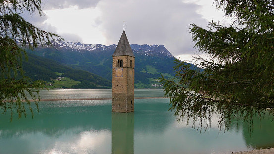 Reservoir Reschensee, South Tyrol, Italy with lone standing steeple in the water, the remaining of flooded village Graun, in early summer with low water level.