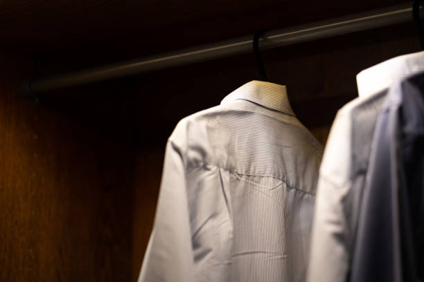 A formal white cotton shirt is hanging in wooden wardrobe. Isolated object and selected focus at the part of T-shirt textile.