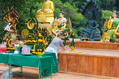 Woman is placing flowers at thai buddhist shrine at Wat Kamchanod in Udon Thani province. There are several statues including a black buddha with Nakhon snakes. There are also a statues of a couple. Man is at right side of Buddha and woman at left side. Wat Kamchanod is popular temple for love prayers