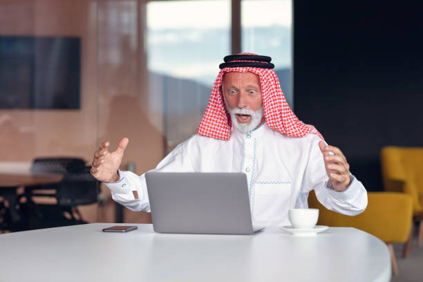 el hombre de negocios árabe se ve sorprendido mientras usa un portátil - headscarf islam senior adult east fotografías e imágenes de stock