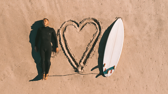 Top view of a man surfer in wetsuit with a surfboard lying on the sand on the beach. I love surf. I love surfing, . High quality photo