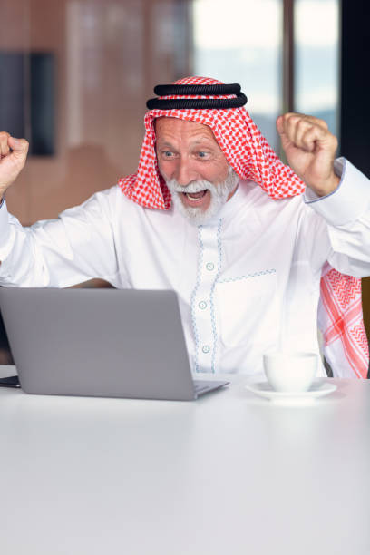 empresário árabe comemorando a vitória no cargo usando laptop. - headscarf islam senior adult east - fotografias e filmes do acervo