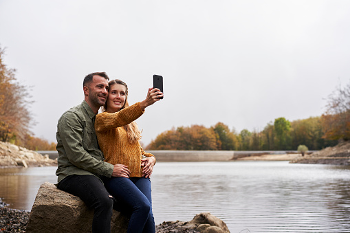Couple sitting in front of the lake doing a selfie.