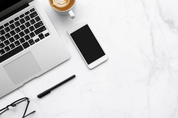 istock White marble office desk table with laptop computer, smartphone with blank screen, cup of latte coffee and office supplies. Top view with copy space, flat lay. 1283183586