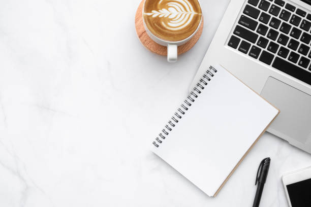 istock White marble office desk table with blank notebook with pen, laptop computer, cup of coffee and supplies. Top view with copy space, flat lay. 1283183659