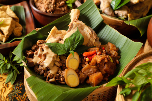 Gudeg Jogja, Javanese Dish of Jackfruit Stew with White Chicken Curry and Cattle Skin Cracker Stew Gudeg Jogja, a Javanesse signature dish of young jackfruit stew; accompanied with white chicken curry and spicy stew of cattle skin cracker. All the dishes are arranged in a bamboo basket as a take-out container. In the background is each of the individual dish that makes up Gudeg Jogja. gudeg stock pictures, royalty-free photos & images