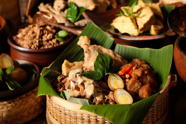 Gudeg Jogja, Javanese Dish of Jackfruit Stew with White Chicken Curry and Cattle Skin Cracker Stew Gudeg Jogja, a Javanesse signature dish of young jackfruit stew; accompanied with white chicken curry and spicy stew of cattle skin cracker. All the dishes are arranged in a bamboo basket as a take-out container. In the background is each of the individual dish that makes up Gudeg Jogja. gudeg stock pictures, royalty-free photos & images